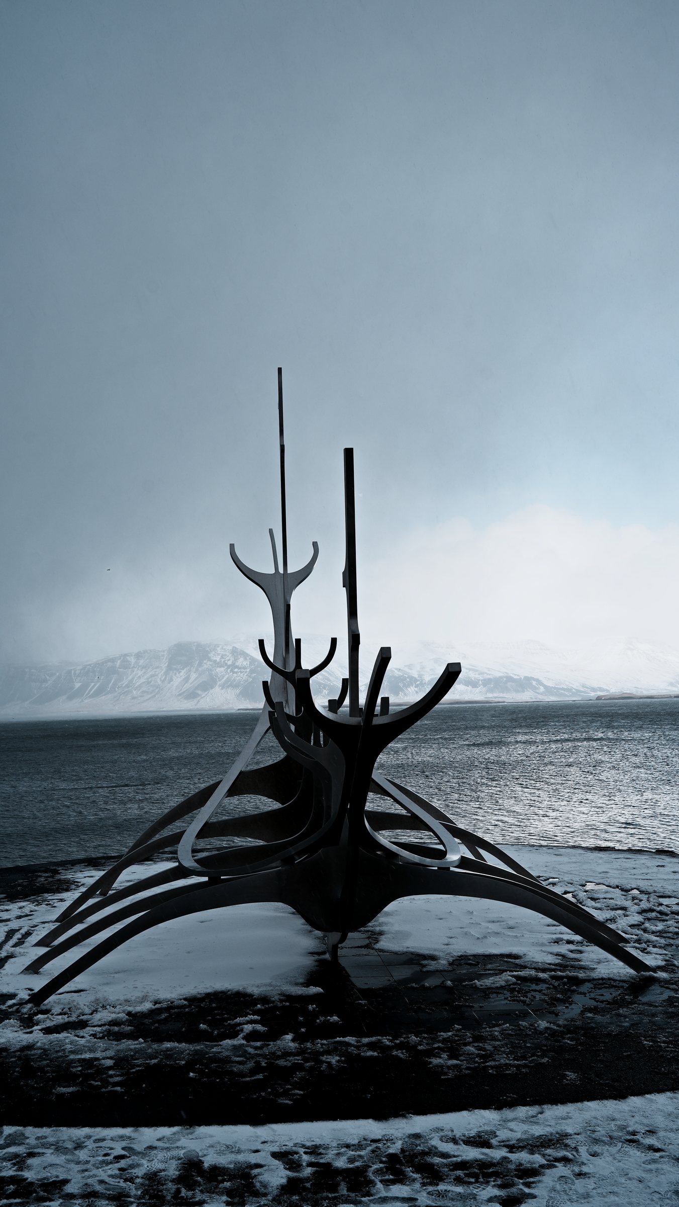 Vertical frame of the Sun Voyager centred under a tall grey sky, the bay and mountains beyond.