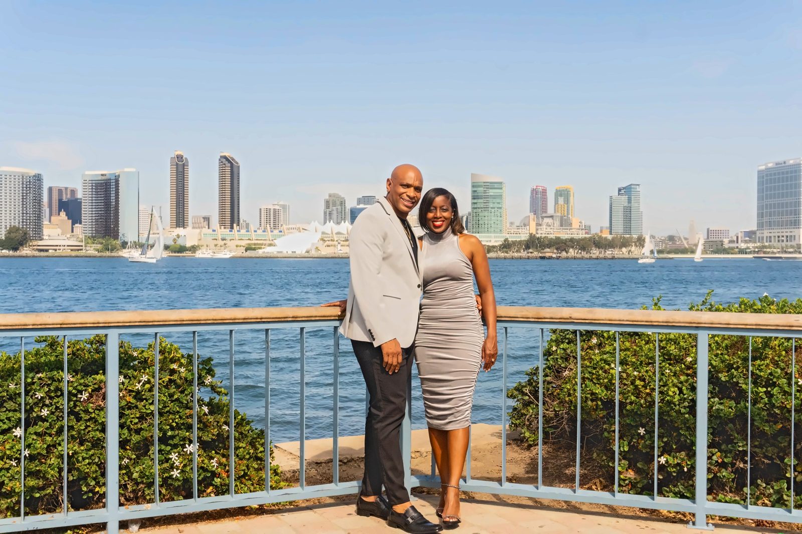Couple standing at the blue railing with skyline and sailboats