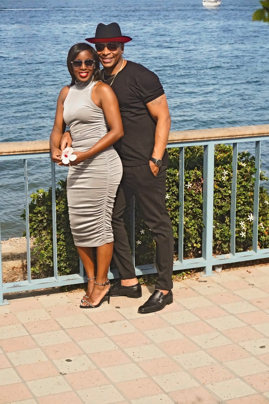 Couple in sunglasses at the railing, she holds a white flower