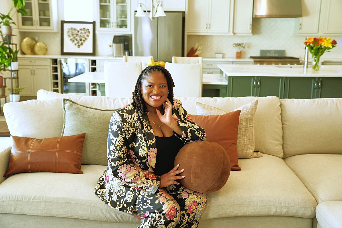Hand to hair, smiling on the sofa with kitchen behind