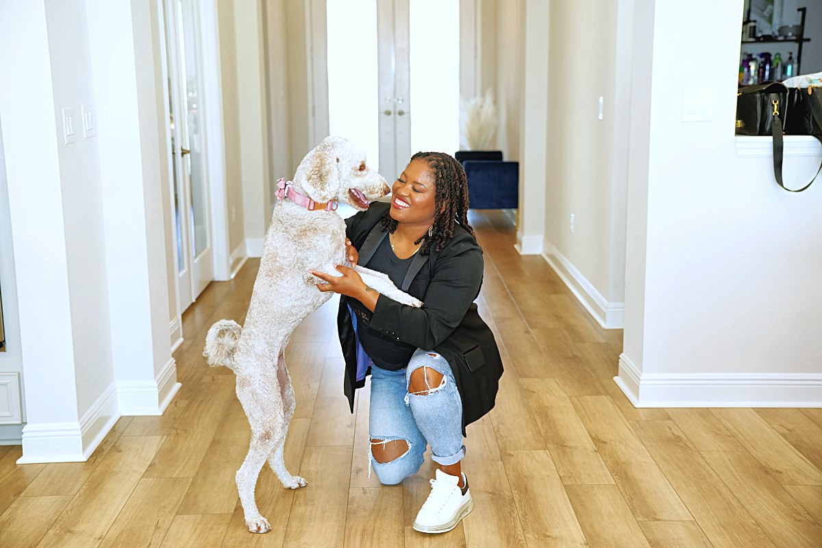 Kneeling as a curly white dog jumps up to greet her