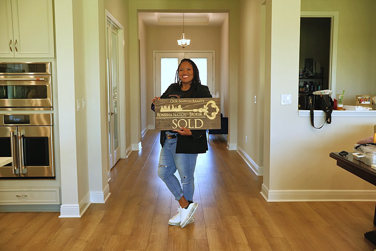Standing at the end of the hallway holding the SOLD sign, kitchen ovens at left